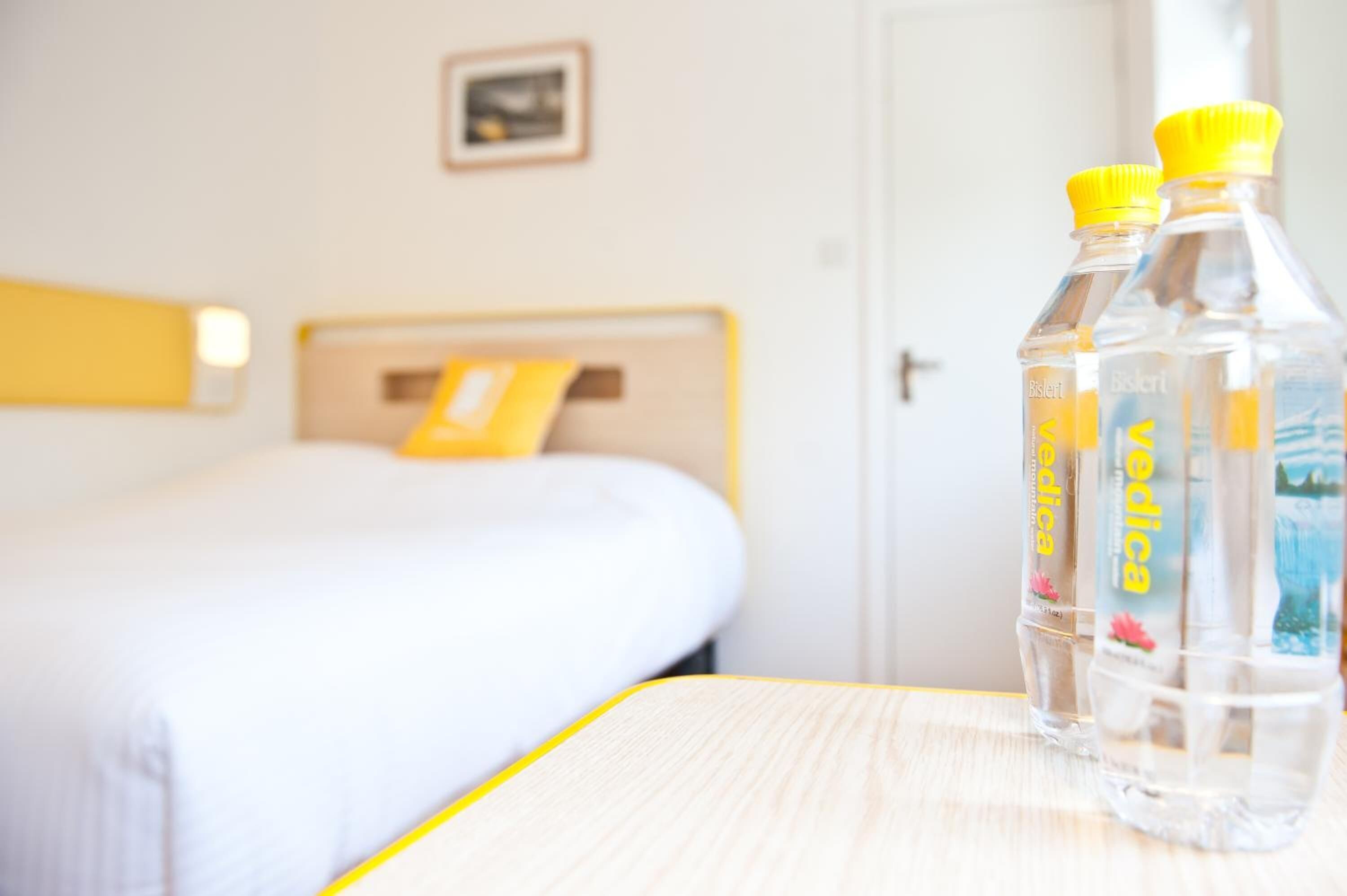 Ett hotellrum med en säng, ett träbord som används som nattduksbord och två flaskor vatten på nattduksbordet.