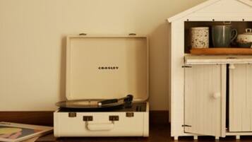 A room with a vintage suitcase, a small white cabinet with kitchenware, and a wooden shelf.