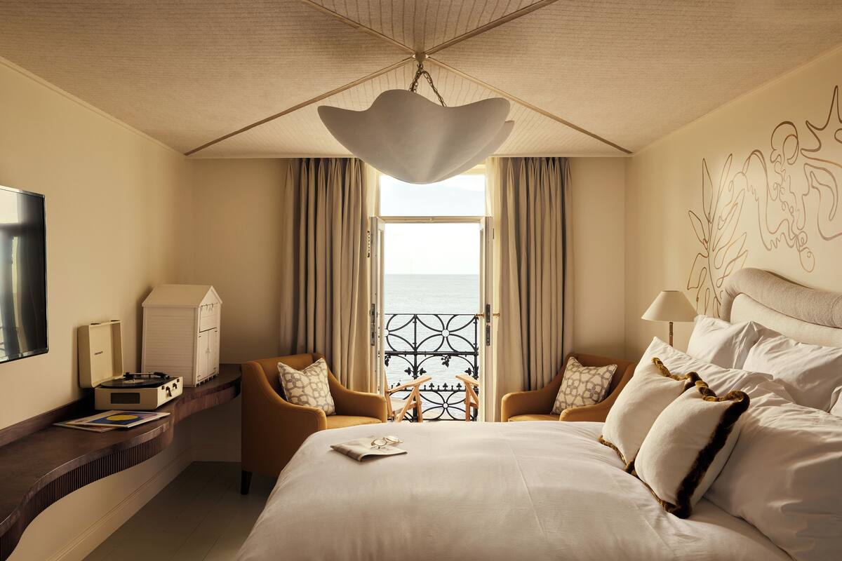 Ett hotellrum med en stor säng, två fåtöljer, ett skrivbord med en platt-TV och utsikt över havet från balkongen.