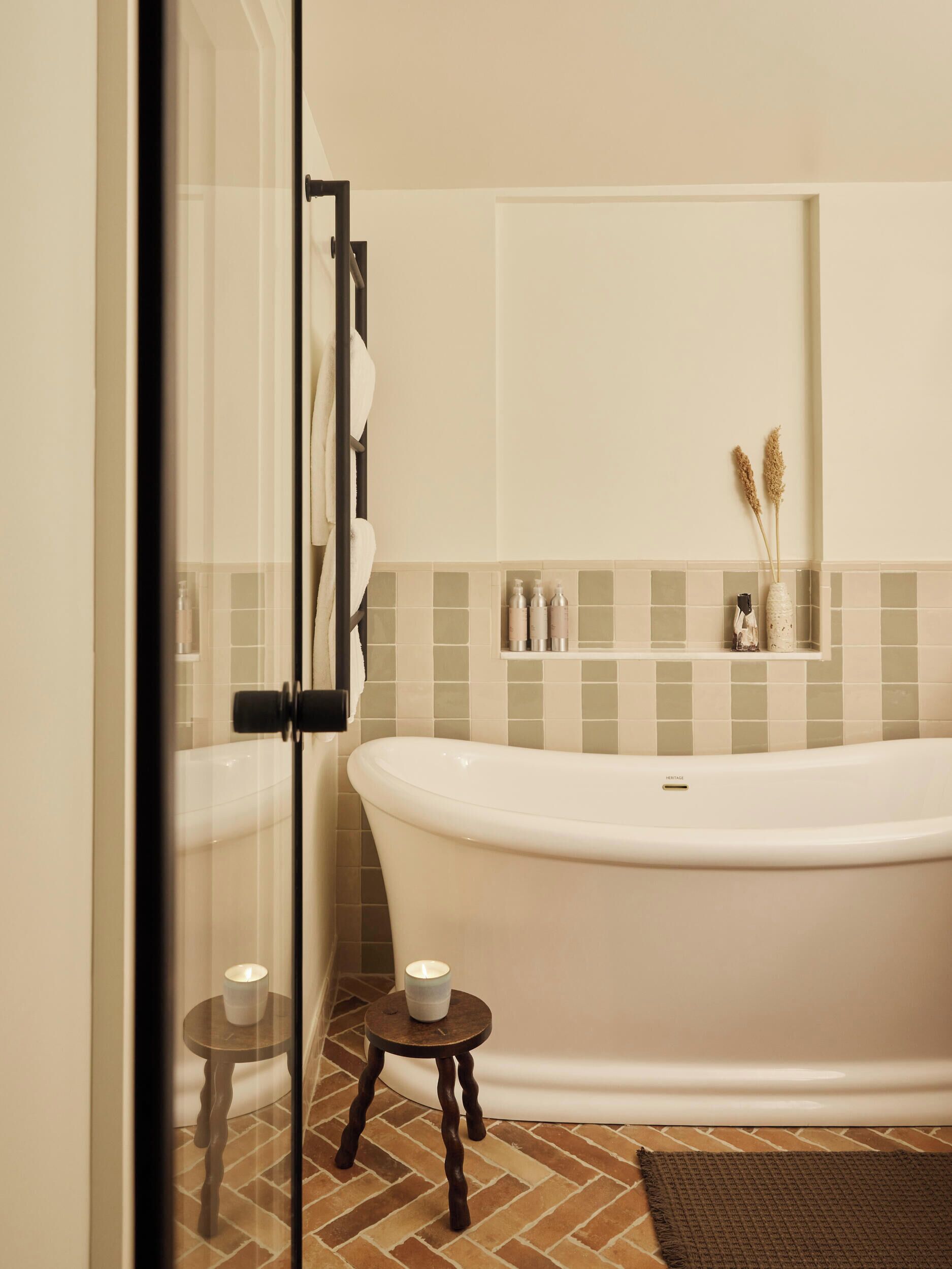 A bathroom with a freestanding bathtub, a glass shower enclosure, and a small wooden stool with two candles.