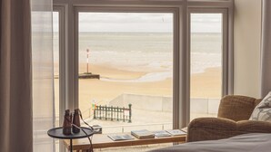 A room with a large window overlooking a beach, a small table with books and binoculars, and a sofa. - No.42 by GuestHouse Margate (Margate)
