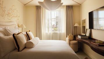 A hotel room with a large bed, a bedside table, a mirror, a TV, and a window with curtains.