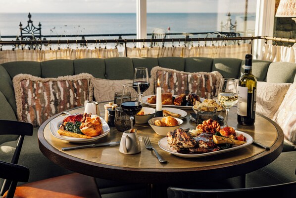 A dining table with plates of food, wine glasses, and a bottle of wine. The table is set on a balcony with a view of the sea. - No.42 by GuestHouse Margate (Margate)