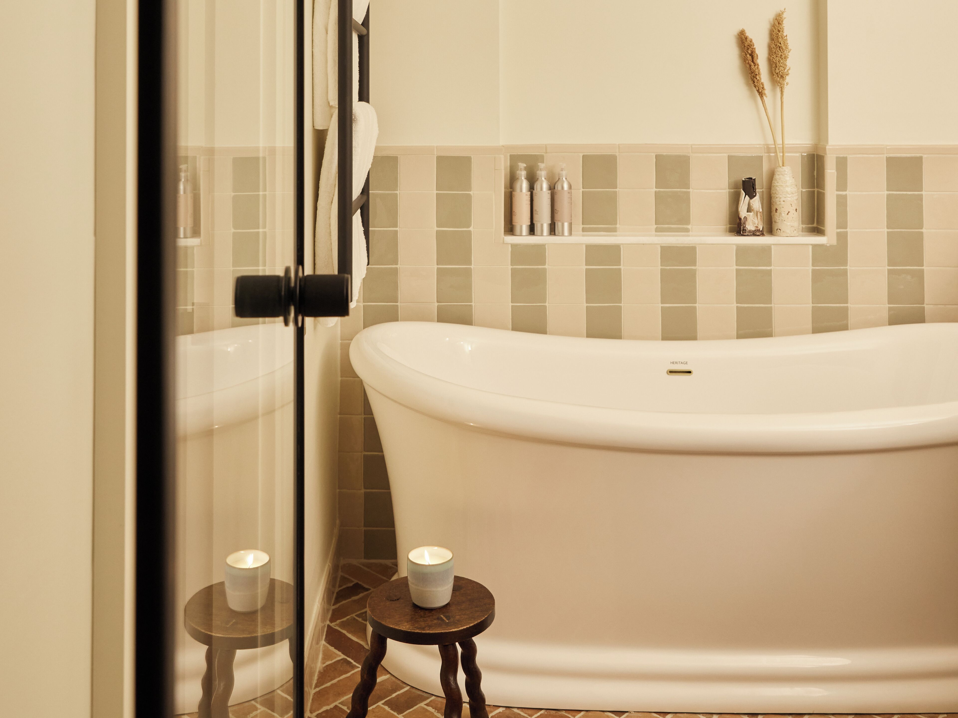 A bathroom with a freestanding bathtub, a glass shower enclosure, and a small wooden stool with a candle.