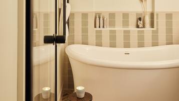 A bathroom with a freestanding bathtub, a glass shower enclosure, and a small wooden stool with a candle.