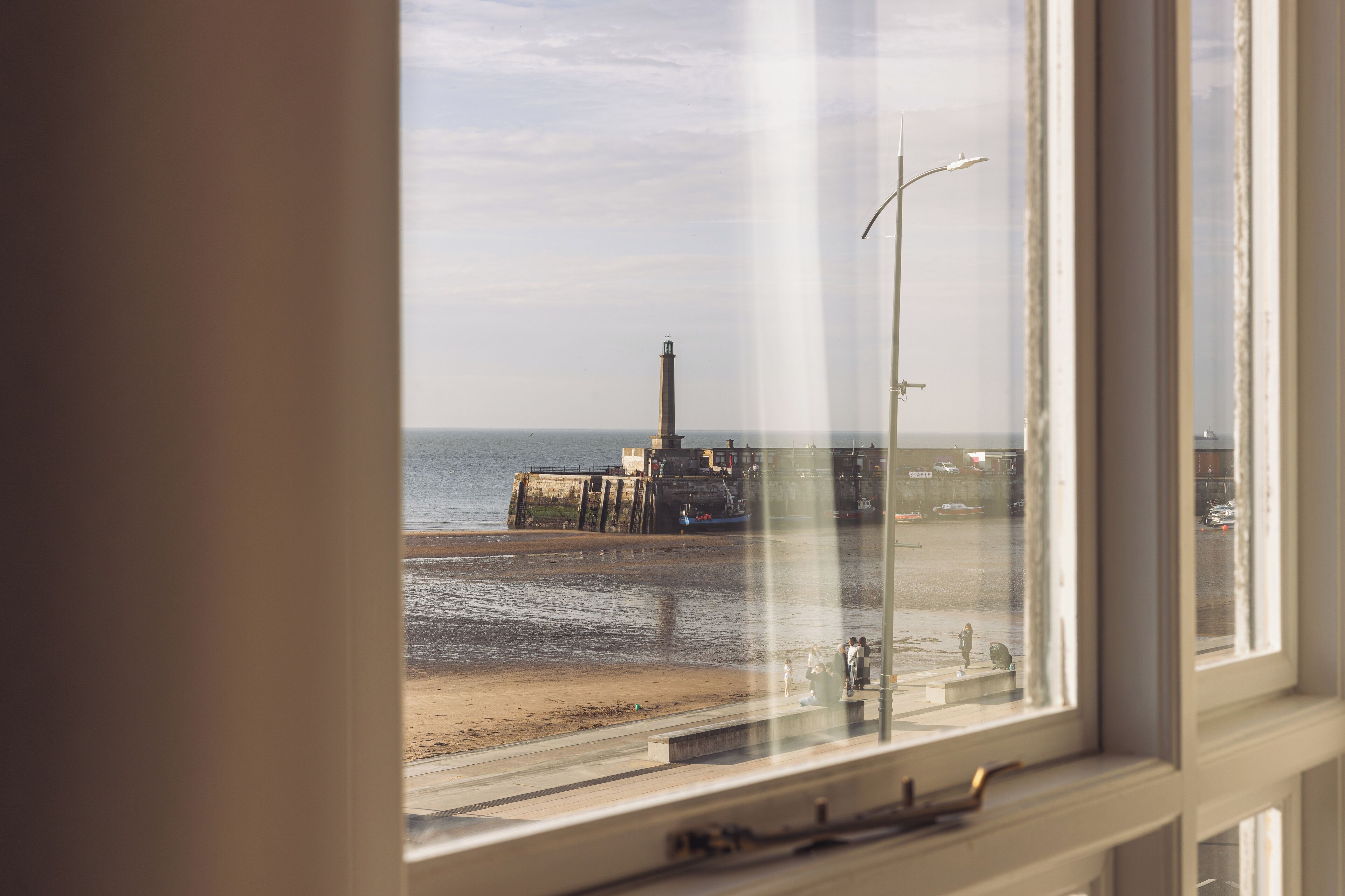 A view from a window overlooking a beach with a lighthouse and a pier.
