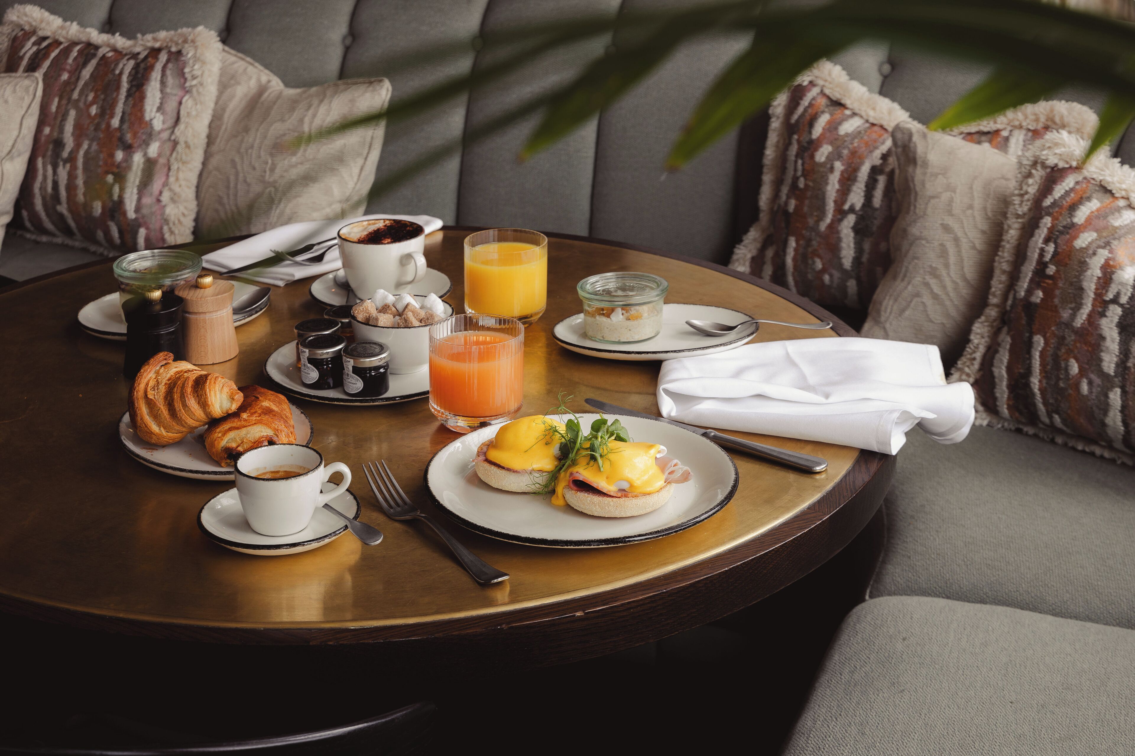 Une table ronde dressée pour le petit-déjeuner, avec des croissants, des œufs, du jus d’orange et du café.