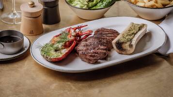 A dining table with a plate of steak, lobster, and vegetables, a bowl of salad, and a glass of red wine.