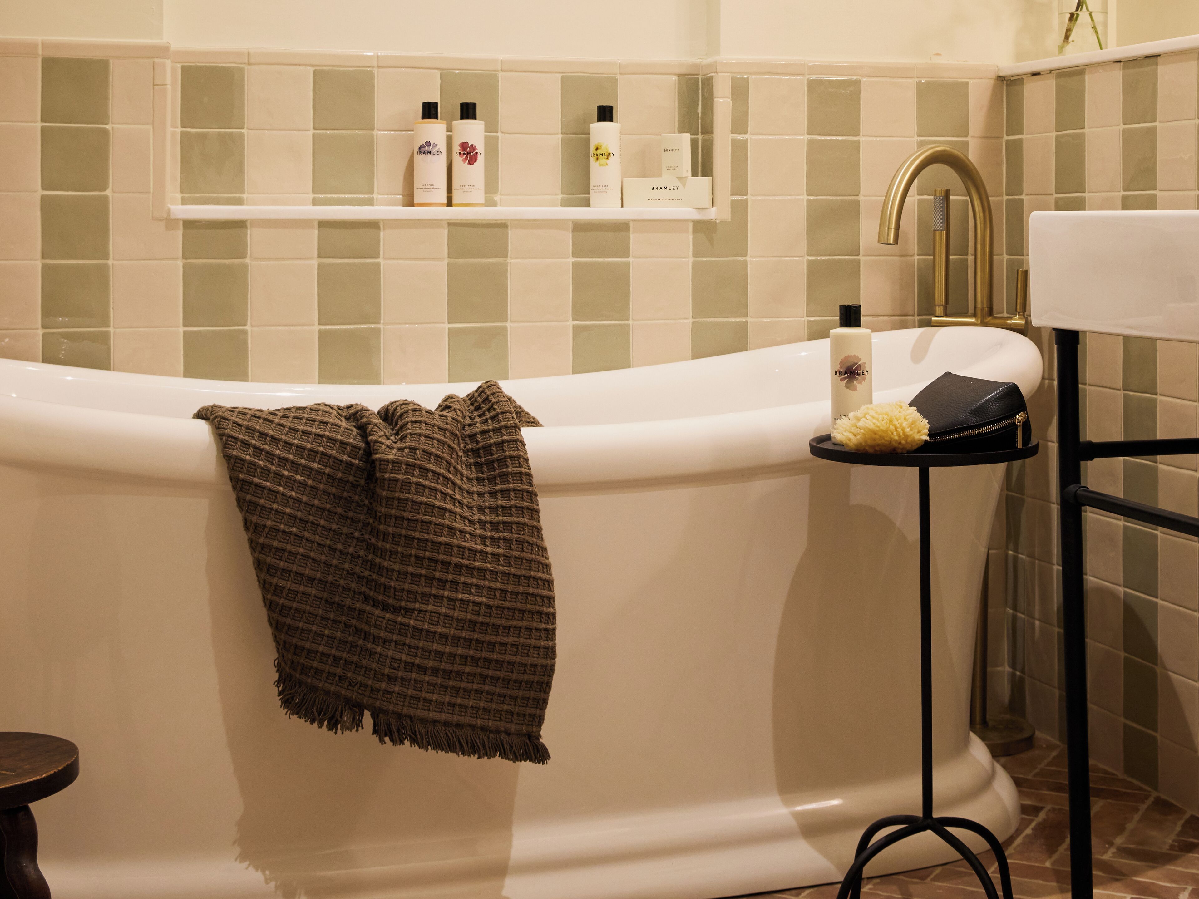 A bathroom with a freestanding bathtub, a towel rack, a shelf with toiletries, and a sink with a gold faucet.