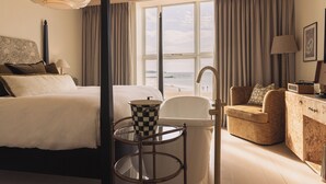 A hotel room with a bed, a sofa, a table with a checkered lamp, a view of the beach, and a large window with curtains. - No.42 by GuestHouse Margate (Margate)