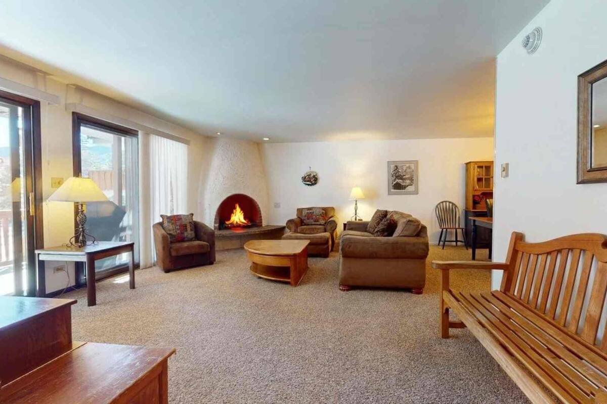 Un salon chaleureux avec une cheminée, des fauteuils confortables et une grande fenêtre.