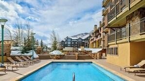 A pool area with lounge chairs, a stone hot tub, and a view of a mountain. - Enzian - CoralTree Residence Collection (Vail)
