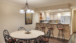 A dining area with a round table and six chairs, a chandelier, and a kitchen in the background. - Enzian - CoralTree Residence Collection (Vail)
