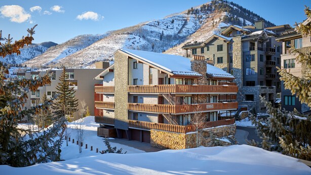 A multi-story hotel with balconies, a stone facade, and a view of a snow-covered mountain. - Enzian - CoralTree Residence Collection (Vail)