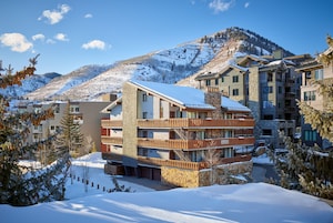 Un hotel de varios pisos con balcones, fachada de piedra y vistas a una montaña nevada.