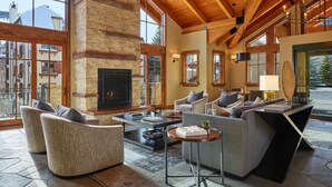 A spacious living area with a fireplace, comfortable seating, and large windows offering a view of the outside. - Enzian - CoralTree Residence Collection (Vail)