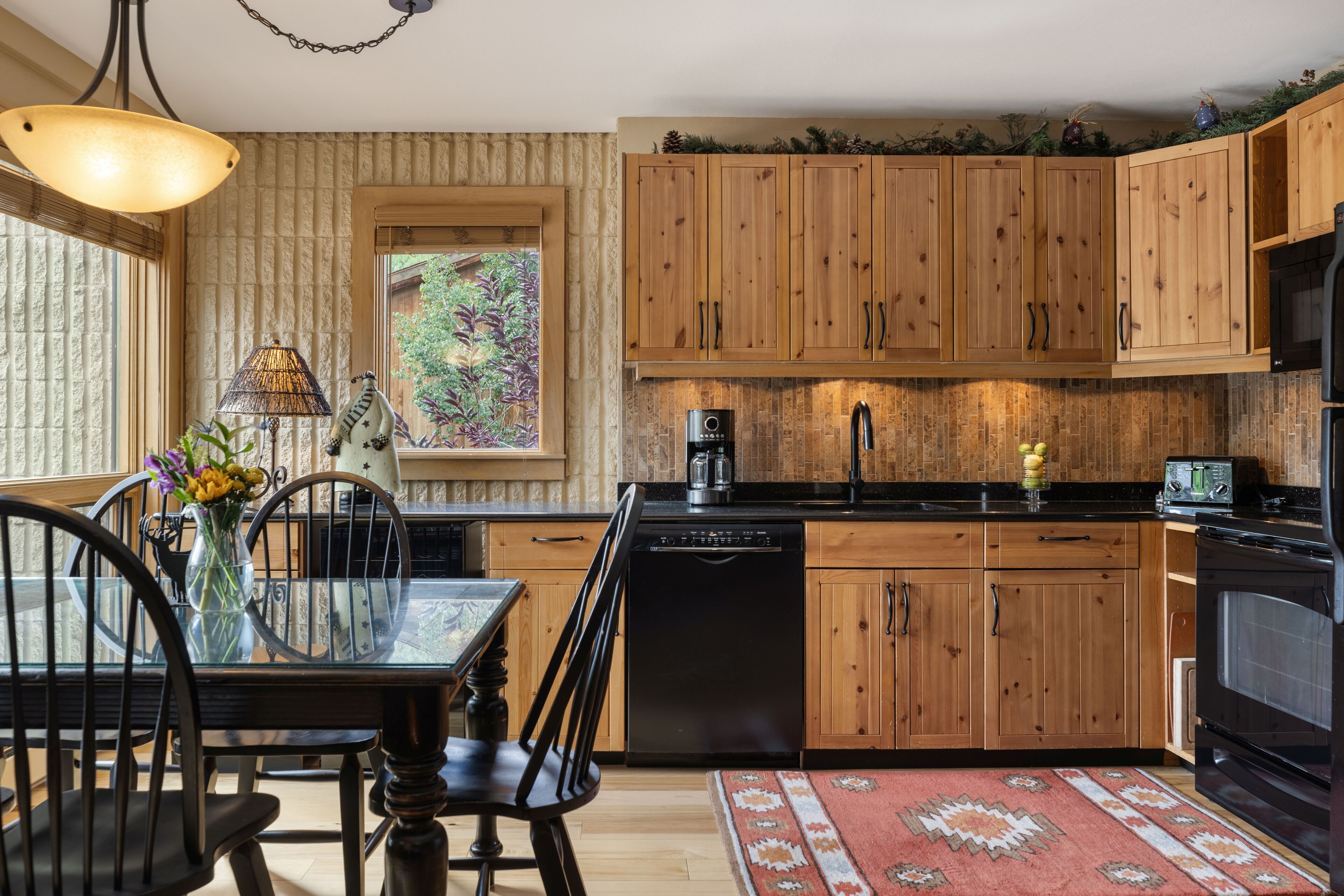 A kitchen with wooden cabinets, a dishwasher, a coffee maker, and a dining area with a table and chairs.