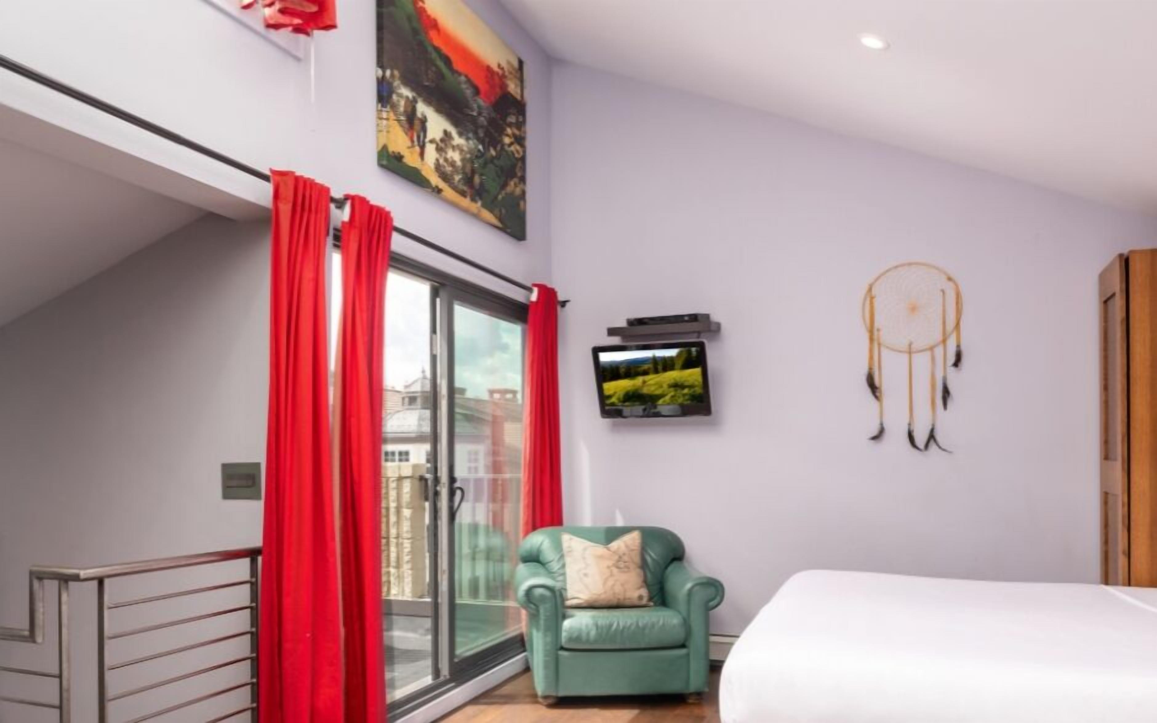 Un dormitorio moderno con un sillón verde, una cama, un atrapasueños y un televisor en la pared.