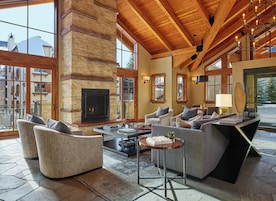 A spacious living area with a stone fireplace, comfortable seating, and large windows offering views of the outside.