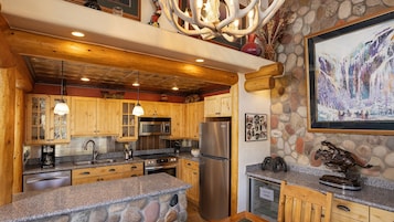 A rustic kitchen with wooden cabinets, granite countertops, a stainless steel refrigerator, and a stone island.