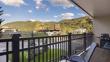 A balcony with a view of a mountainous landscape, a traditional building, and a barbecue grill.