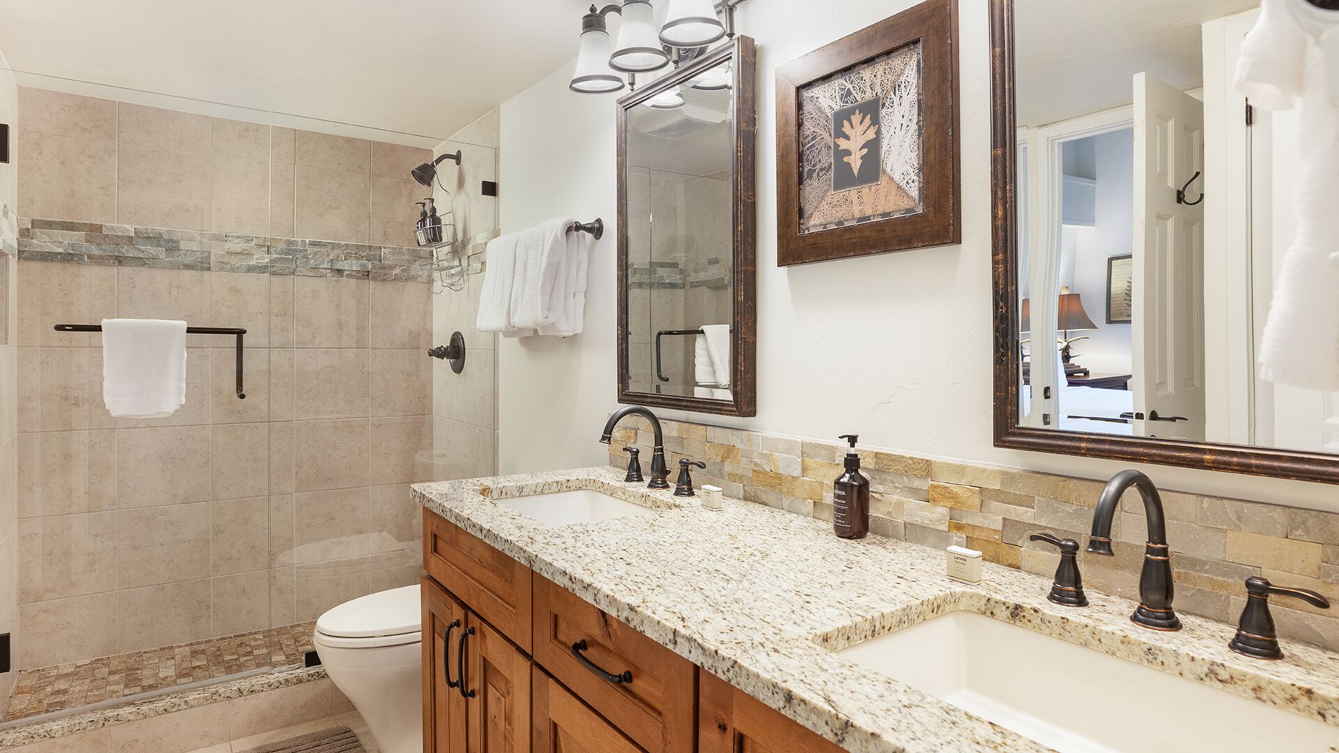 A bathroom with a shower, a toilet, a vanity with a sink, and two mirrors.