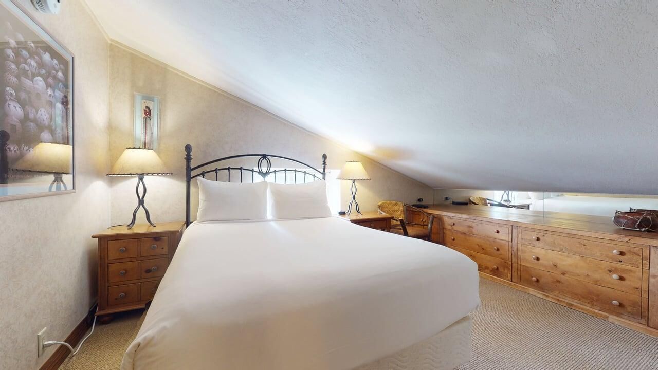 A bedroom with a bed, wooden dresser, two bedside lamps, and a mirror.