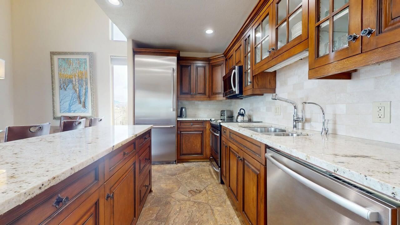 Una cocina con armarios de madera, encimeras de granito, electrodomésticos de acero inoxidable y salpicadero de azulejos.