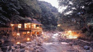 A traditional Japanese ryokan with a stone pathway leading to a wooden bridge over a flowing stream. - Pension Asanebou (Minakami)