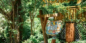 Un letrero de madera con caracteres japoneses, rodeado de abundante follaje y una valla de madera.