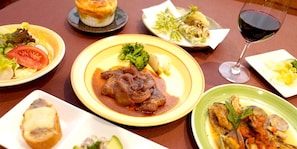Una mesa con varios platos, incluyendo carne y verduras, una copa de vino tinto y otros platos con distinta comida.