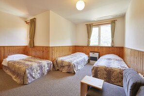 Una habitación con tres camas individuales, paneles de madera, una ventana con cortinas y una mesita.