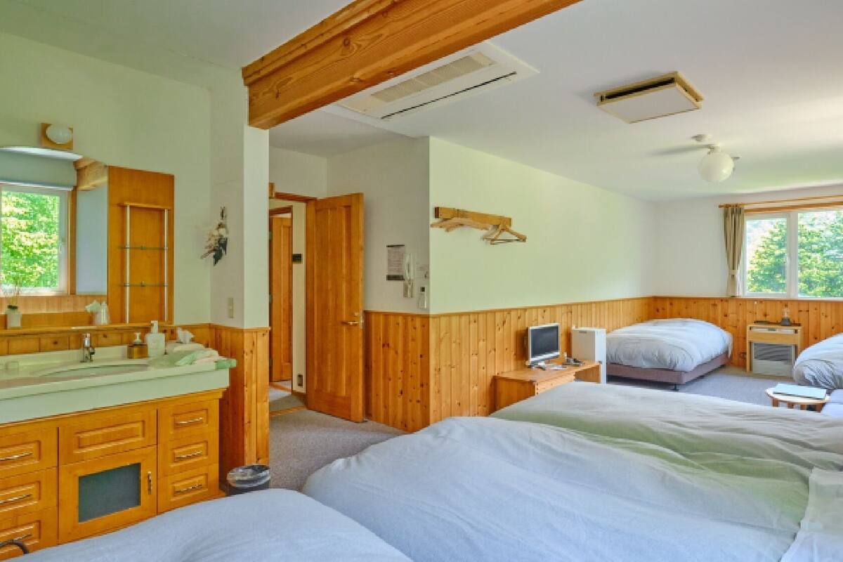 A room with wooden paneling, a large mirror, a sink, two beds, a TV, and a window with curtains.