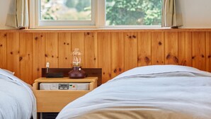A bedroom with two beds, wooden paneling, a nightstand with a lamp, and a window with curtains. - Pension Asanebou (Minakami)