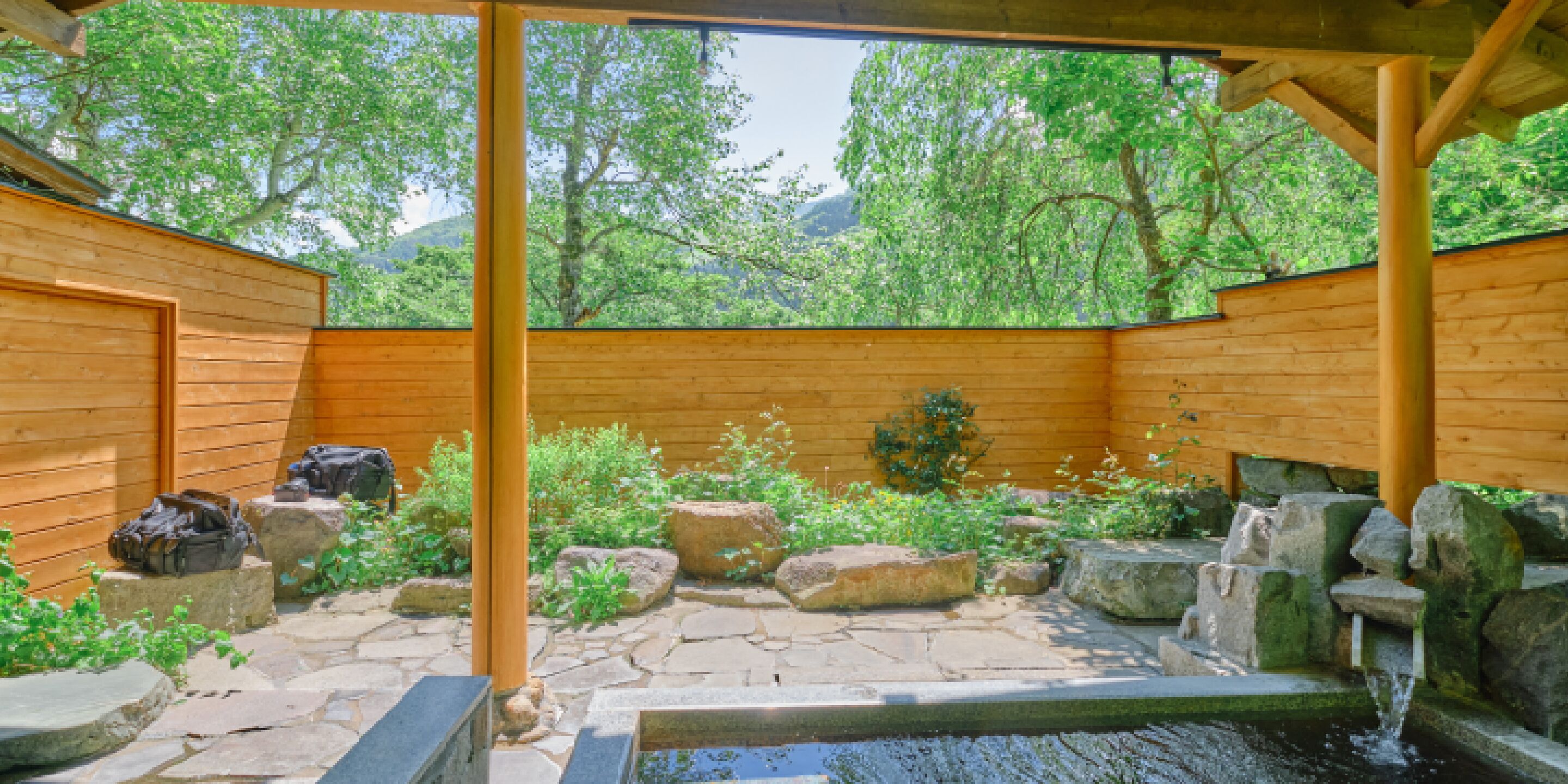 A wooden cabin with a stone patio, a small pond, and surrounding greenery.