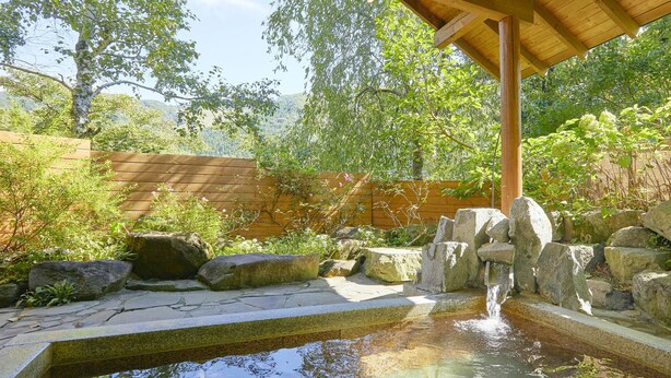 A stone water feature with a wooden pergola overhead, surrounded by rocks and greenery. - Pension Asanebou (Minakami)