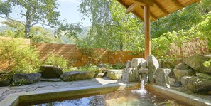 A stone water feature with a wooden pergola overhead, surrounded by rocks and greenery. - Pension Asanebou (Minakami)