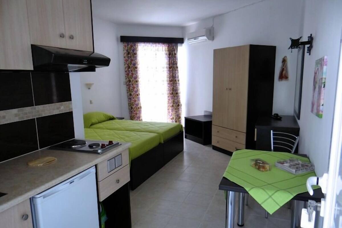 A compact room with a bed, kitchenette, and a small dining table.