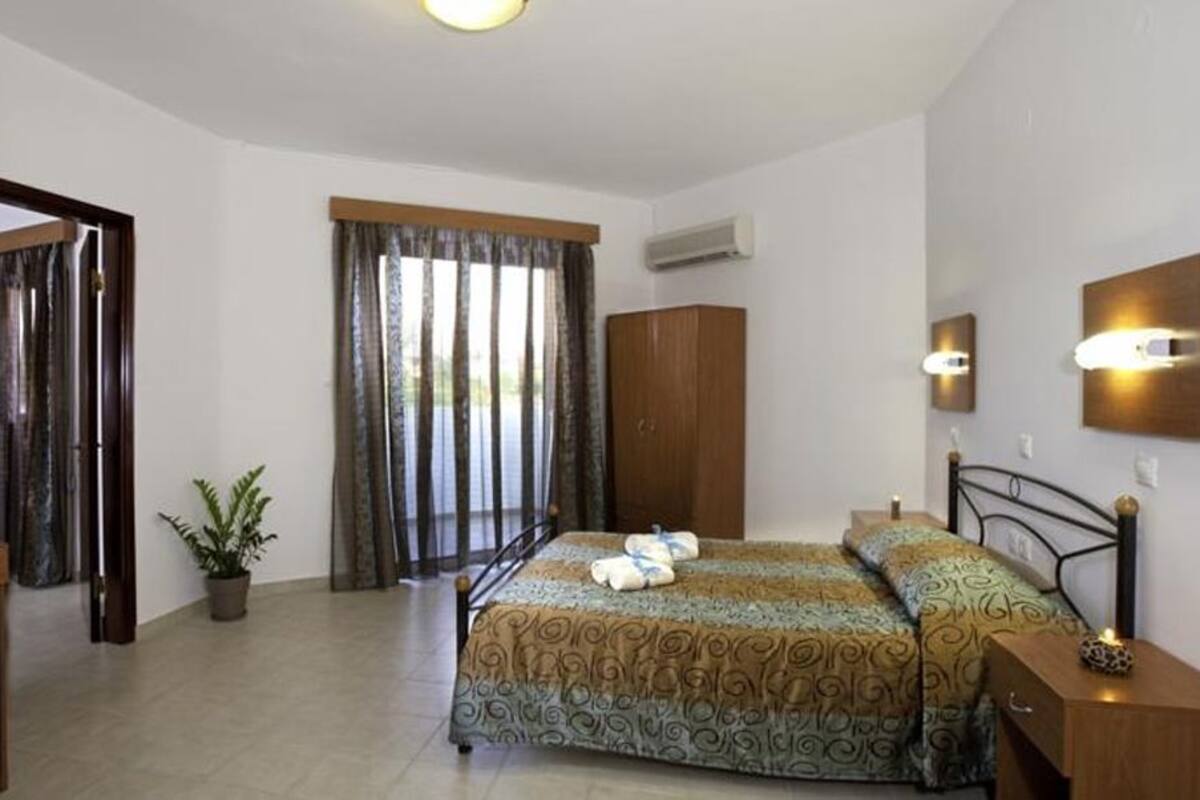 A bedroom with a bed, a desk, a wardrobe, and a potted plant.