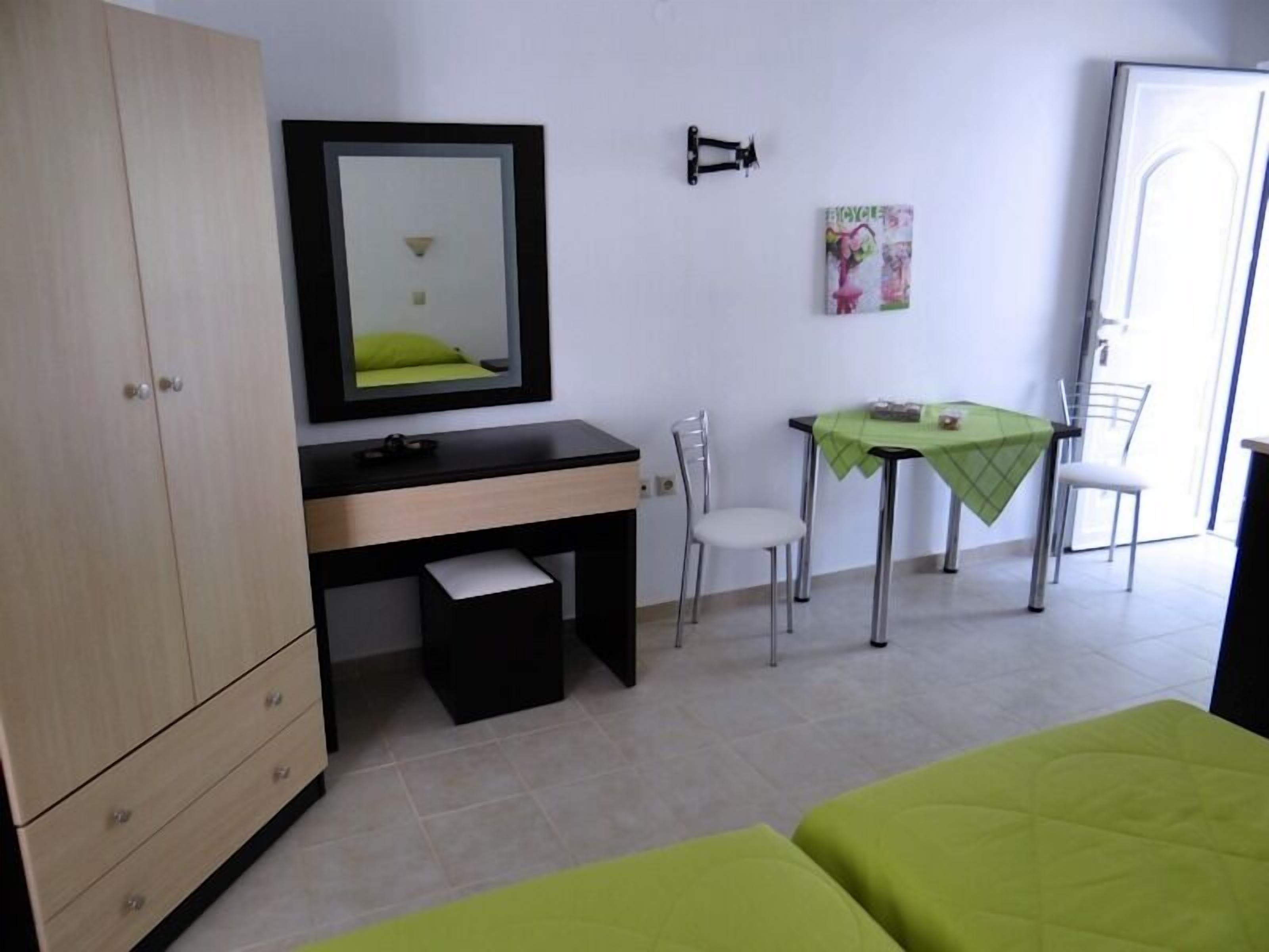 A bedroom with a bed, a desk, a chair, a wardrobe, and a small table with a green tablecloth.