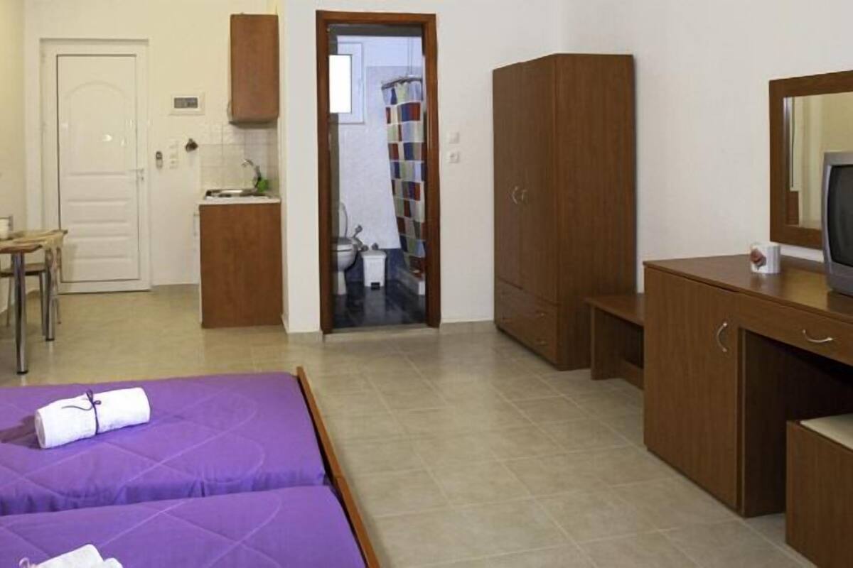 A hotel room with two beds, a desk, a chair, a television, and a bathroom visible through an open door.