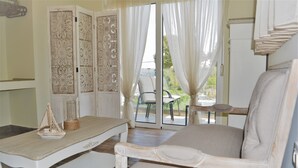 Une pièce avec une table blanche, une chaise blanche et une vue sur l’extérieur par une porte vitrée.