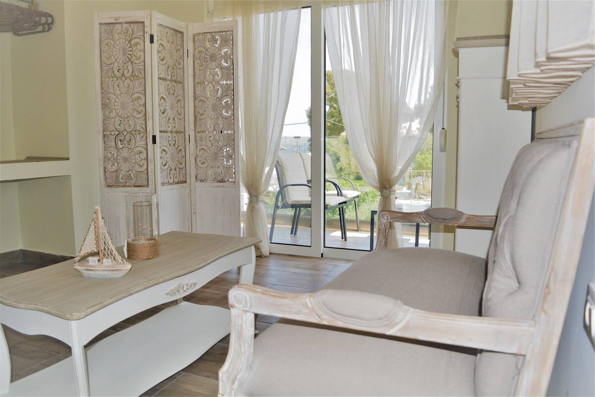 A room with a white table, a white chair, and a view of the outdoors through a glass door.