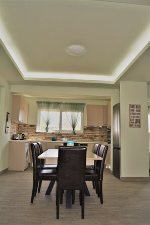 A compact kitchen with a dining area. It includes a table with chairs, a refrigerator, and a window with curtains. - Anelia Boutique Studios & Apartments (Rhodes)