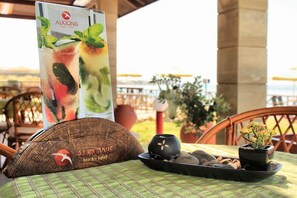 A table with a menu, a wooden bowl, a small potted plant, and a tray with stones and shells. - Alkionis Beach Hotel Apartments (Rethymnon)