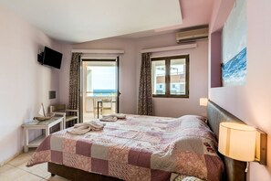 A bedroom with a bed, a TV, a desk, and a chair. There is a balcony with a view of the sea. - Alkionis Beach Hotel Apartments (Rethymnon)