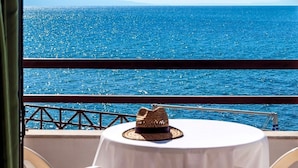 A table with a hat on it, overlooking a bright blue sea with a railing in the foreground. - Alkionis Beach Hotel Apartments (Rethymnon)