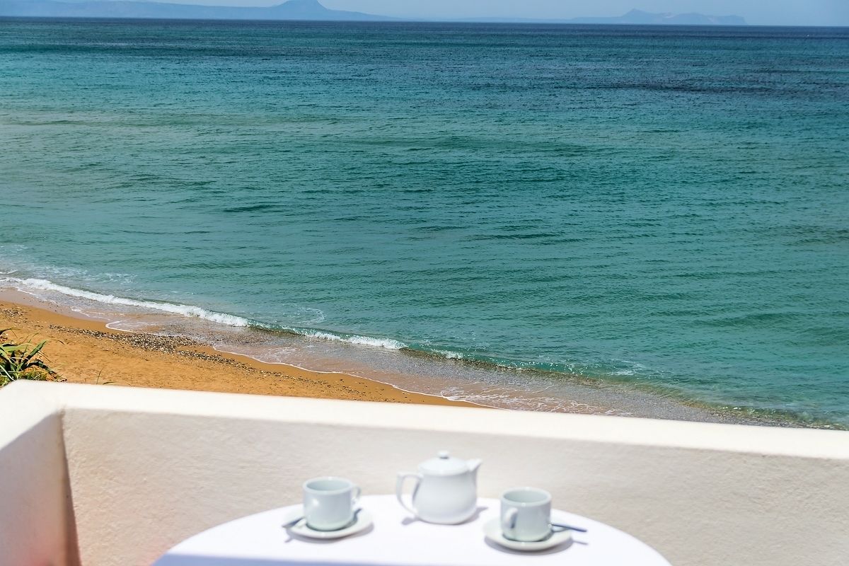 Un balcón con una mesa dispuesta para tomar té, con vistas a una playa y al mar.