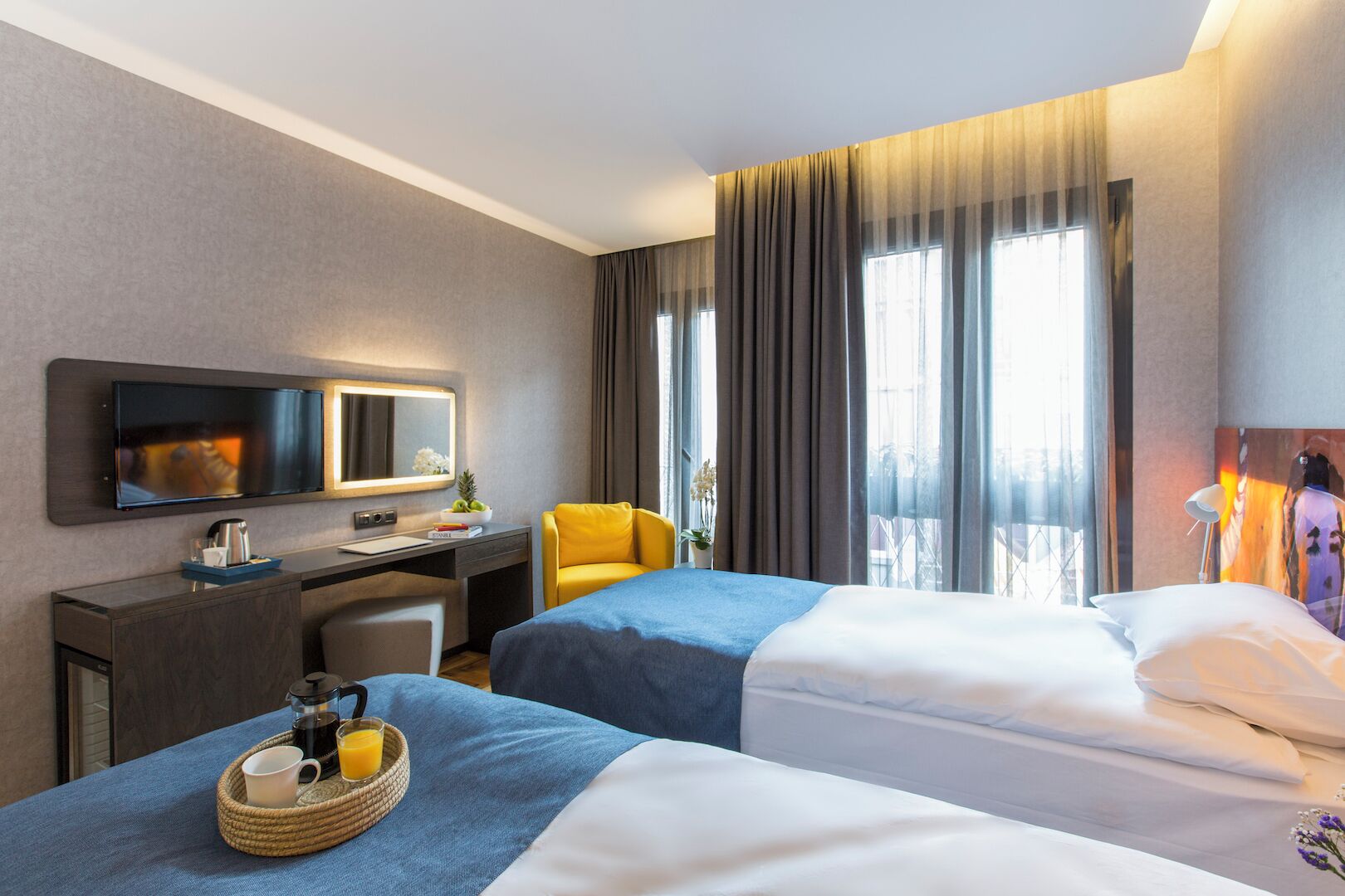 Habitación de hotel con dos camas, un escritorio con computadora, una silla y un ventanal con cortinas.