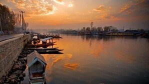 A calm river with boats docked along the shore, a stone wall, and a bridge in the background. - Lily of Nageen (Srinagar)